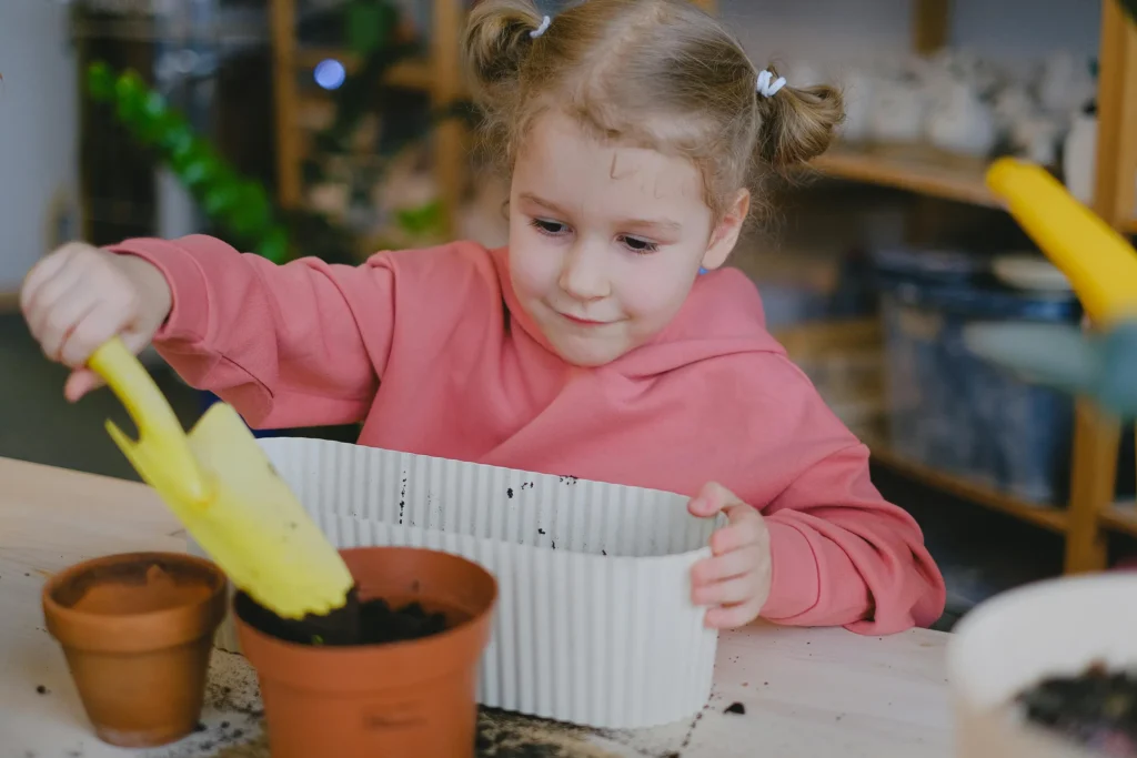 Niña pequeño llenando maceta de barro con sustrato y tierra para huerto